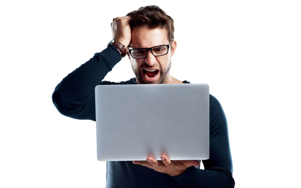 یک مرد عینکی که از کندی و هنگ کردن لپتابش عصبانی شده